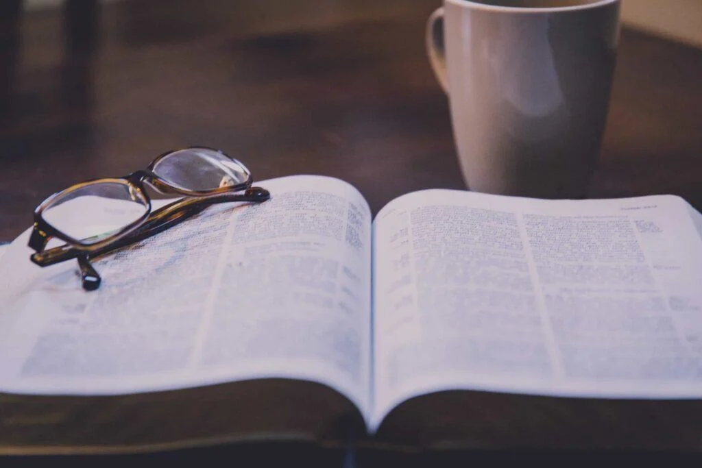 Open Bible with reading glasses on top and a coffee mug in the background, inspirational faith image.