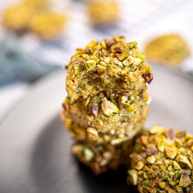 Close-up of pistachio-topped cookies on a white plate with blurred background.