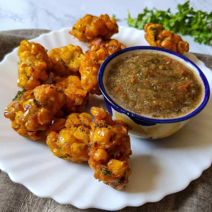 Close-up of crispy Indian-style fritters with spicy chutney on a white plate.