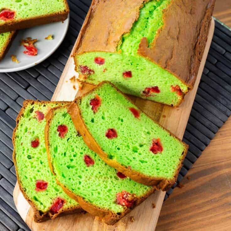 Bright green cherry cake slices on wooden board with red cherries inside.