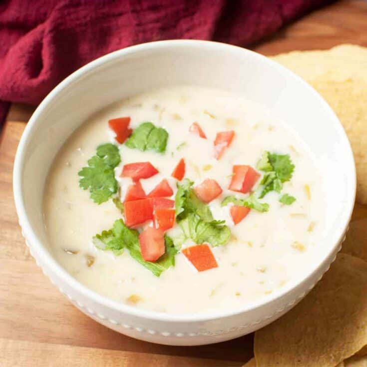 Bowl of creamy soup garnished with cilantro and diced tomatoes on a wooden table.