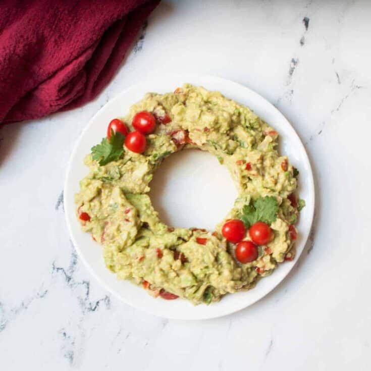 Guacamole served in a ring shape with cherry tomatoes and cilantro on a white plate.