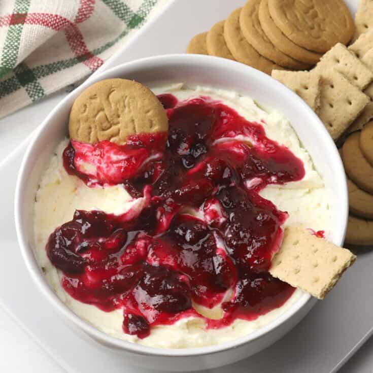 Cream cheese dip with cherry topping and assorted cookies on a white plate.