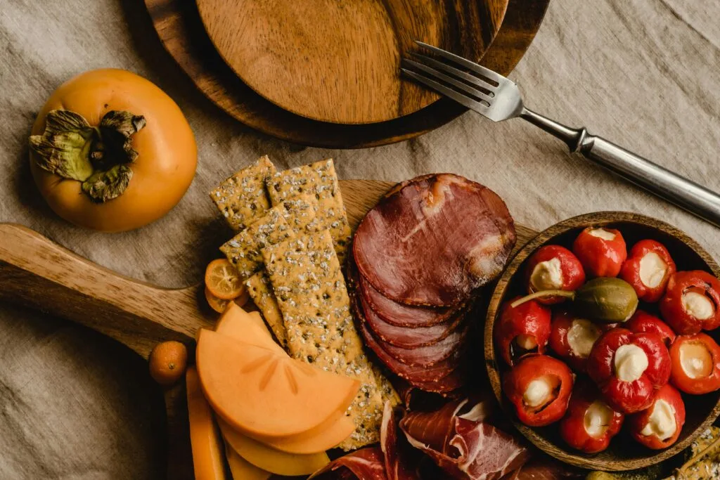 Explore a beautifully arranged fall charcuterie board featuring cured meats, stuffed peppers, crackers, and fruits. 