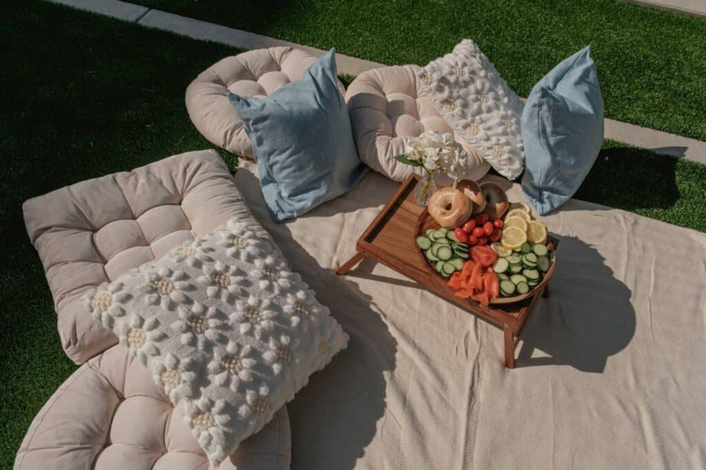 Outdoor picnic setup with cushions, pillows, and food tray