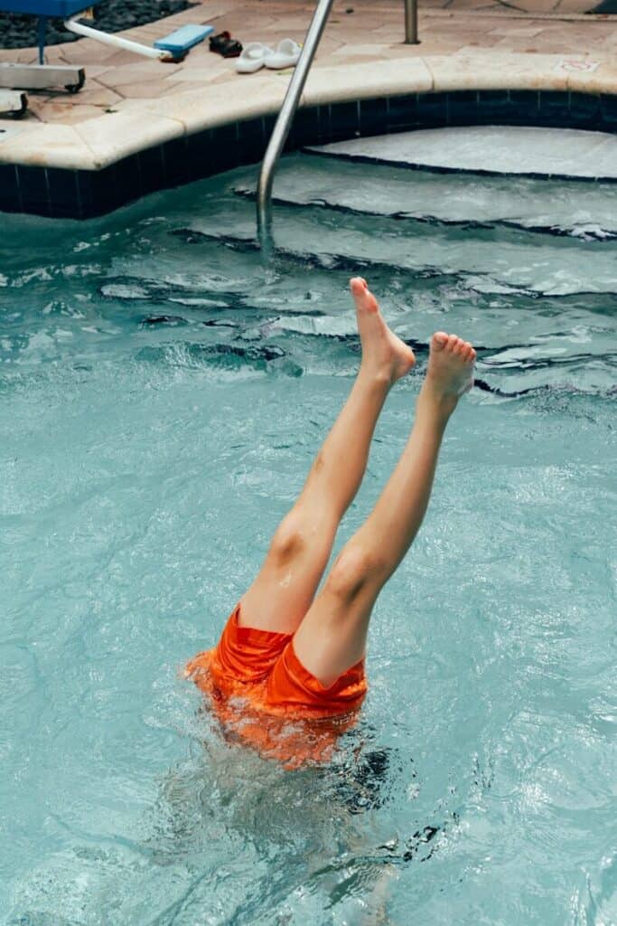 Child with orange shorts upside down in pool