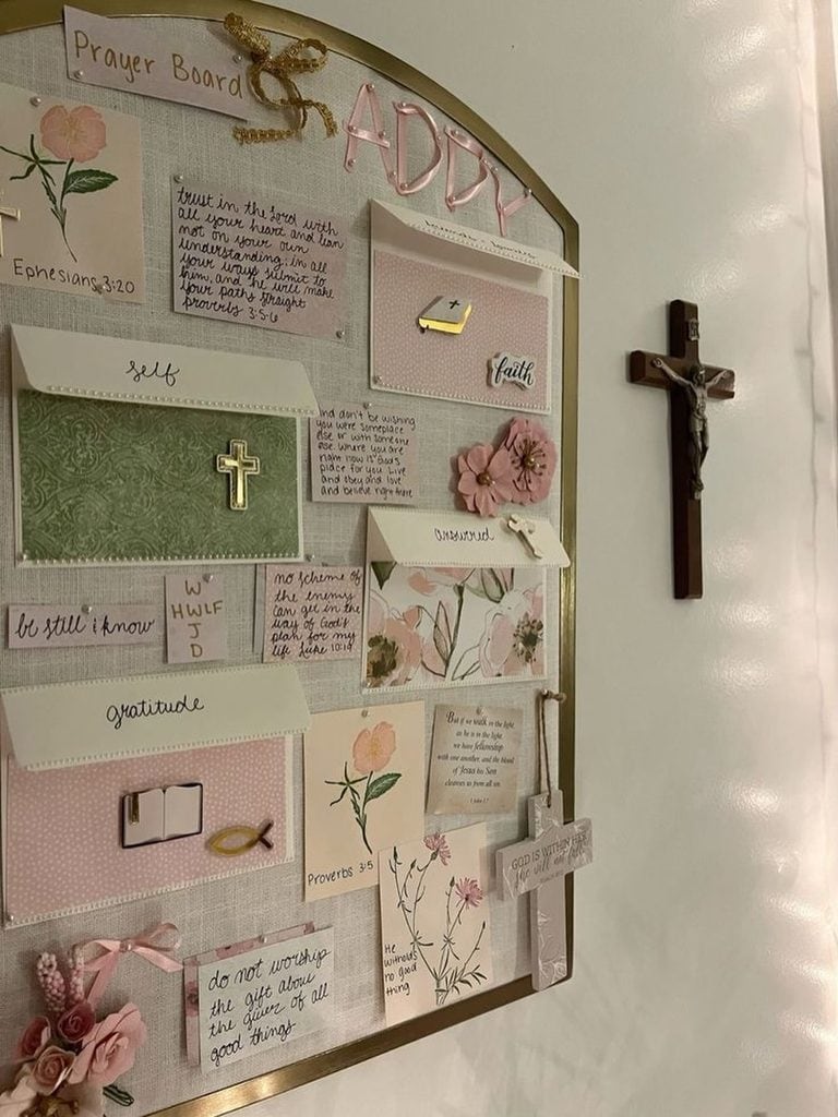Prayer board with faith-themed notes, cross, and floral decorations in a church setting.