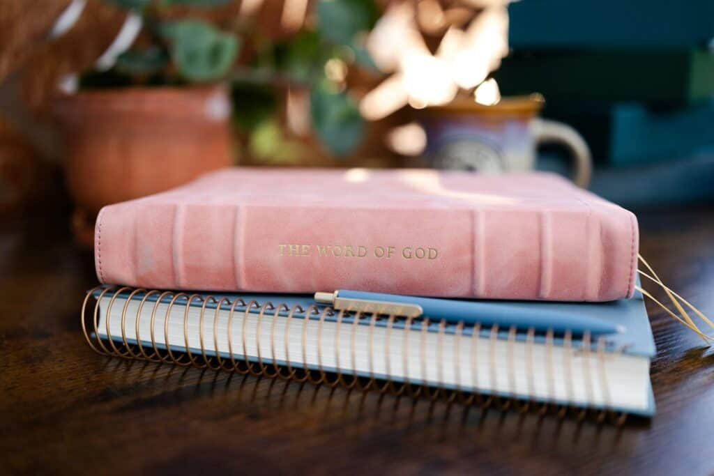 A pink leather book titled "THE WORD OF GOD" on a blue spiral notebook