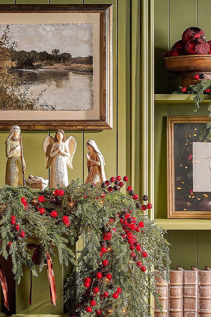 Festive Christmas nativity scene with greenery and red berries on a green wall.