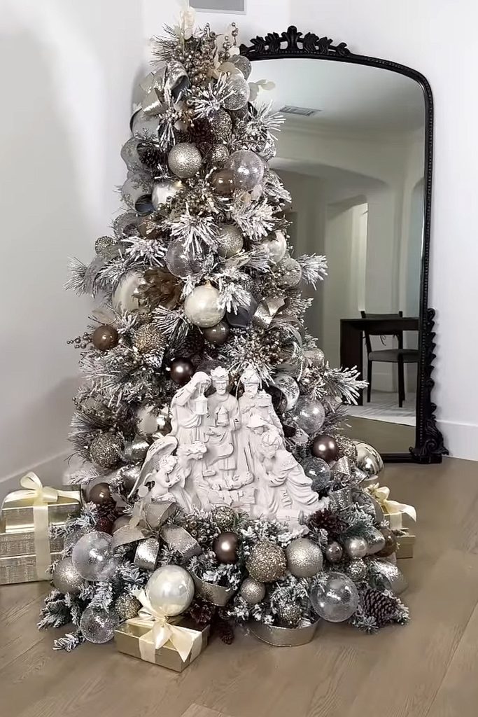 Silver and gold Christmas tree with ornaments and nativity scene at base.